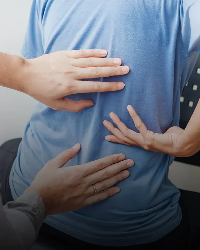 A patient reaches for their back in pain. A doctor examines the spot that the patient is indicating.