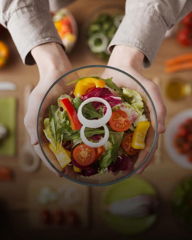 Two hands hold a salad bowl full of colorful veggies like lettuce, peppers, tomatoes, and onions