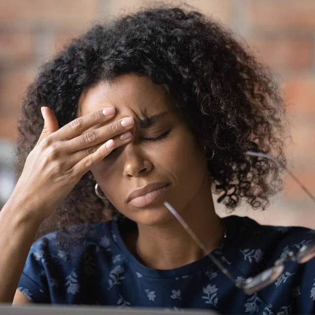 A woman takes off her glasses and rubs her forehead, trying to ease the pain in her head
