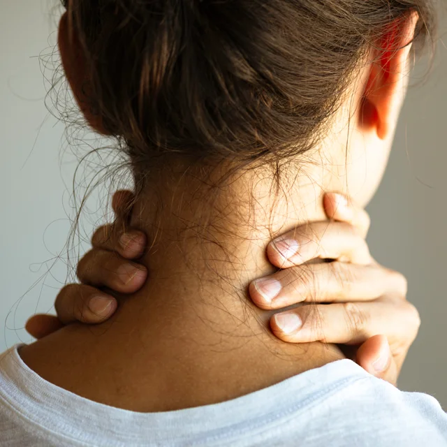 A young woman photographed from the back clutches her neck in pain