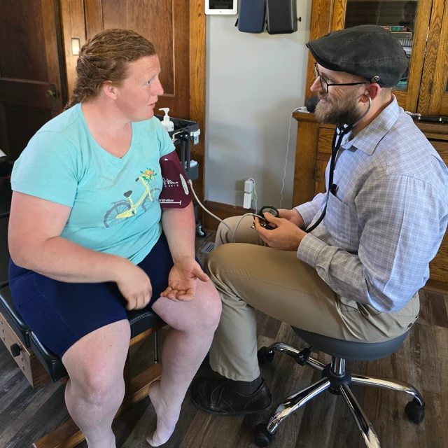 Dr. Jacob Stoffel sits with a patient in his office, taking her blood pressure