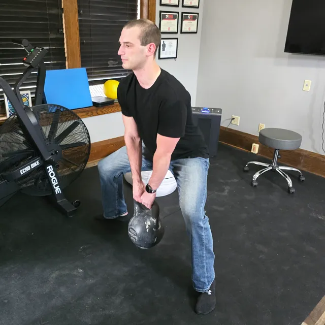 A chiropractic patient performing kettlebell wide leg squats